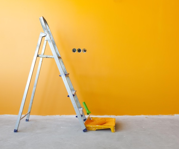 Farbrolle und Leiter stehen vor einer frisch gestrichenen, gelben Wand