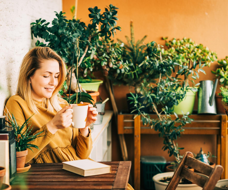 Ein Frau sitzt mit einer Tasse Kaffee auf ihrer Terrasse. 