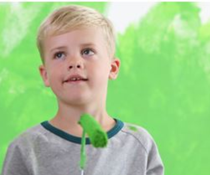 Ein Kind mit grüner Farbe am Hals hinter einer grünen Wand. 