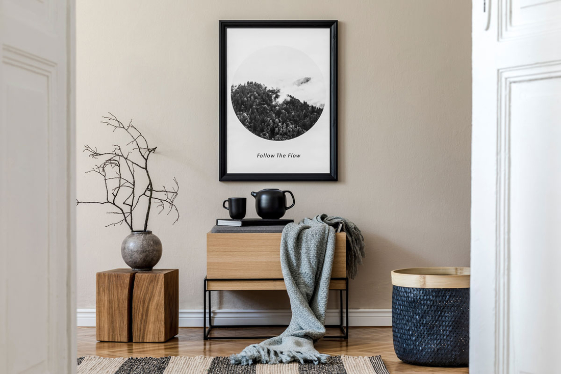 Ein Flur mit beigefarbener Wand, einem Holztisch, darauf schwarze Dekoration und darüber ein Bild mit schwarzem Rahmen. 